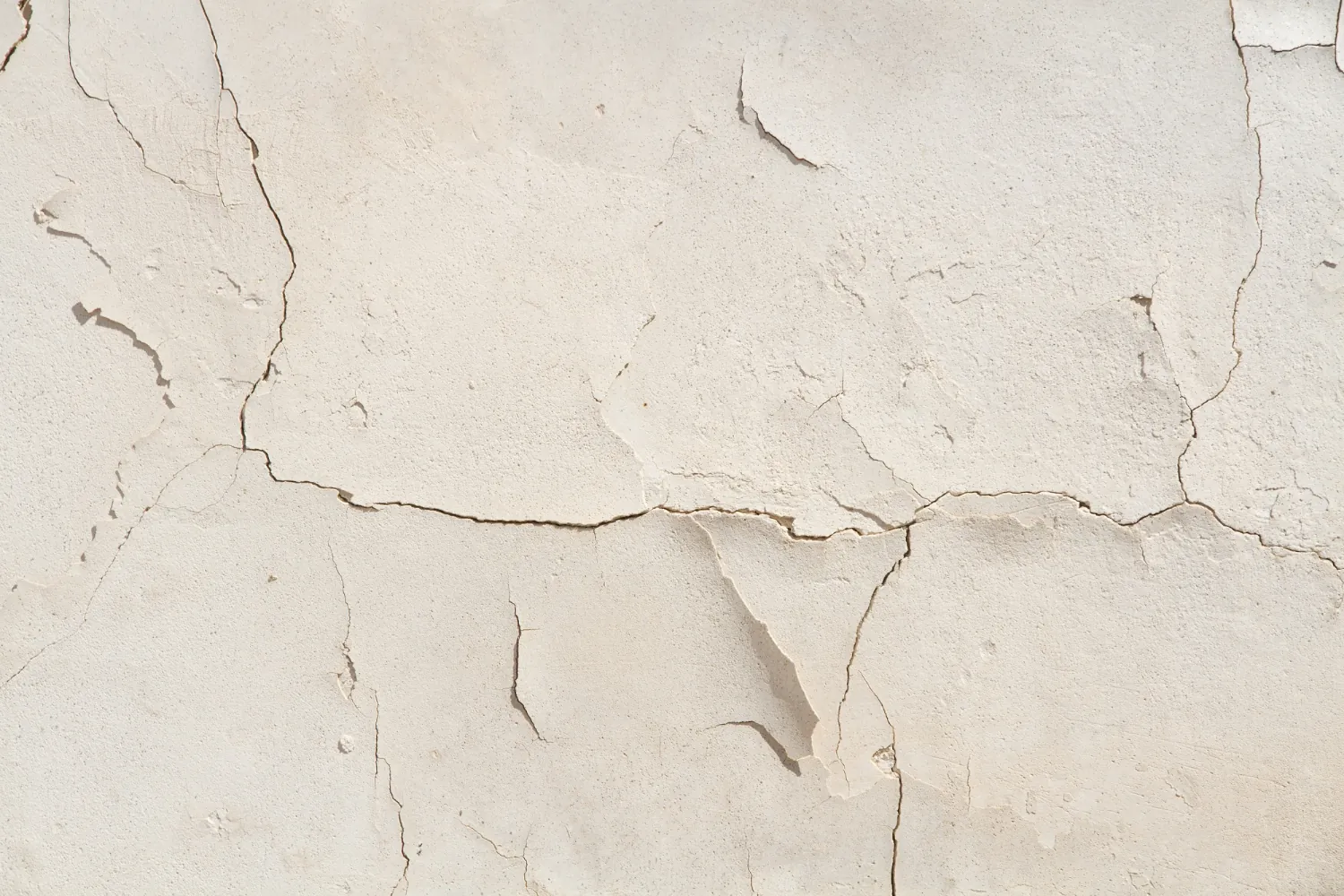 Pared con el tarrajeo blanco cuarteado por varias grietas finas en distintas direcciones