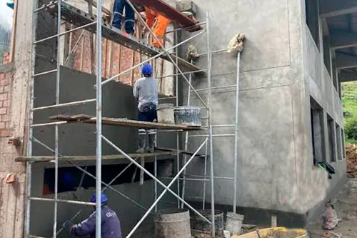 Operarios sobre un andamio metálico tarrajean con cemento la fachada de un edificio de dos pisos