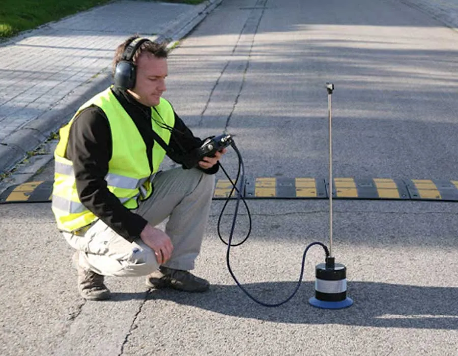 Técnico con audífonos y chaleco reflectante escucha con un geófono apoyado en el pavimento