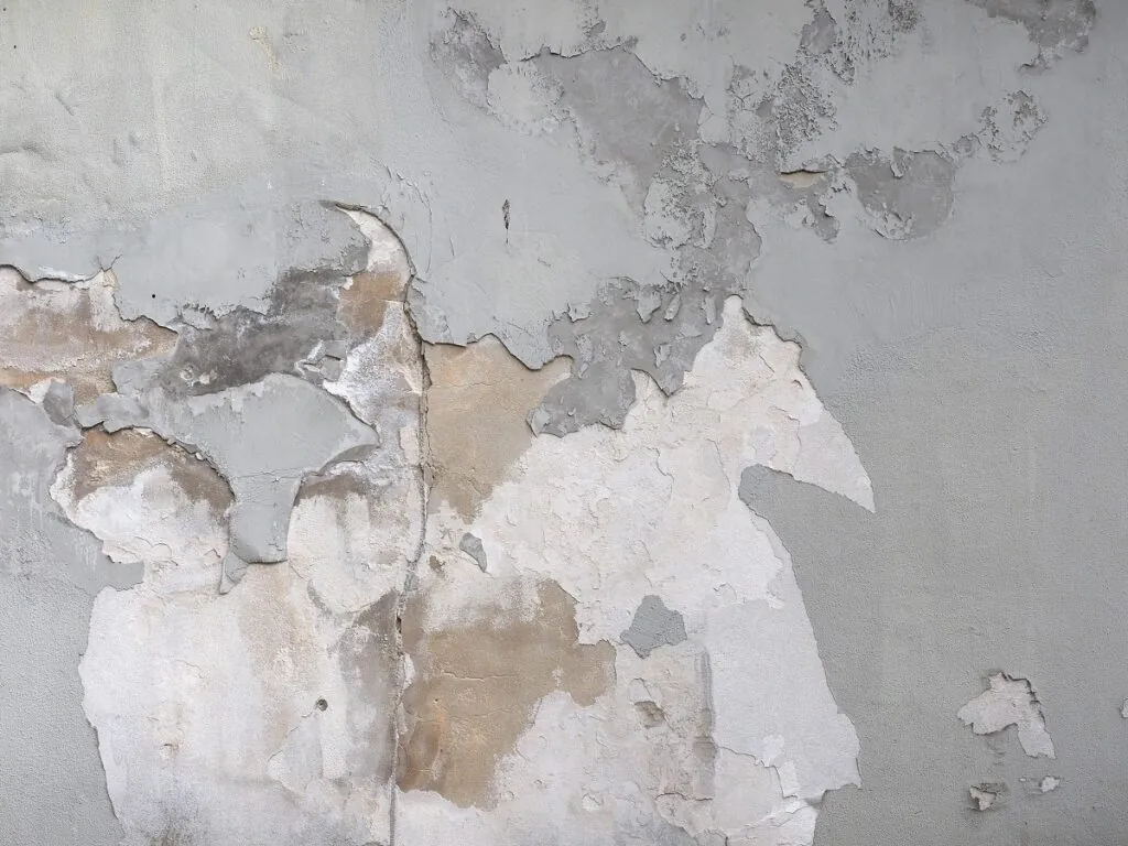Muro con el revoque desprendido por capas, que deja ver manchas y la superficie de abajo
