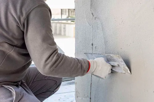 Mano con guante extiende mortero con una llana metálica sobre un muro